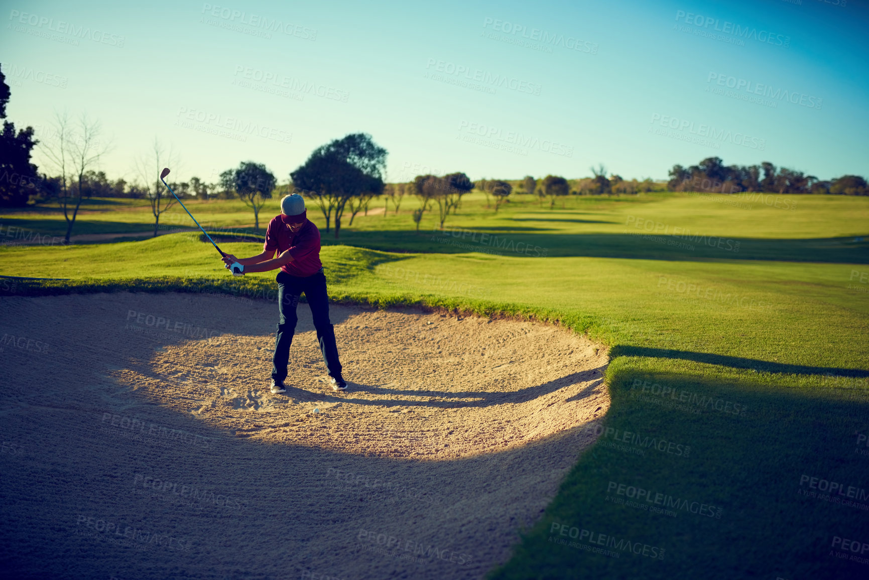 Buy stock photo Shot of a young man hitting the ball out of the bunker during a round of golf