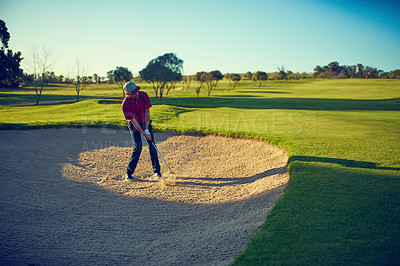 Buy stock photo Shot of a young man hitting the ball out of the bunker during a round of golf