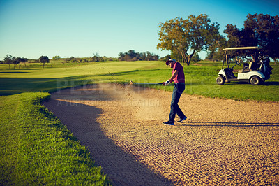 Buy stock photo Shot of a young man hitting the ball out of the bunker during a round of golf