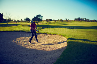 Buy stock photo Shot of a young man hitting the ball out of the bunker during a round of golf