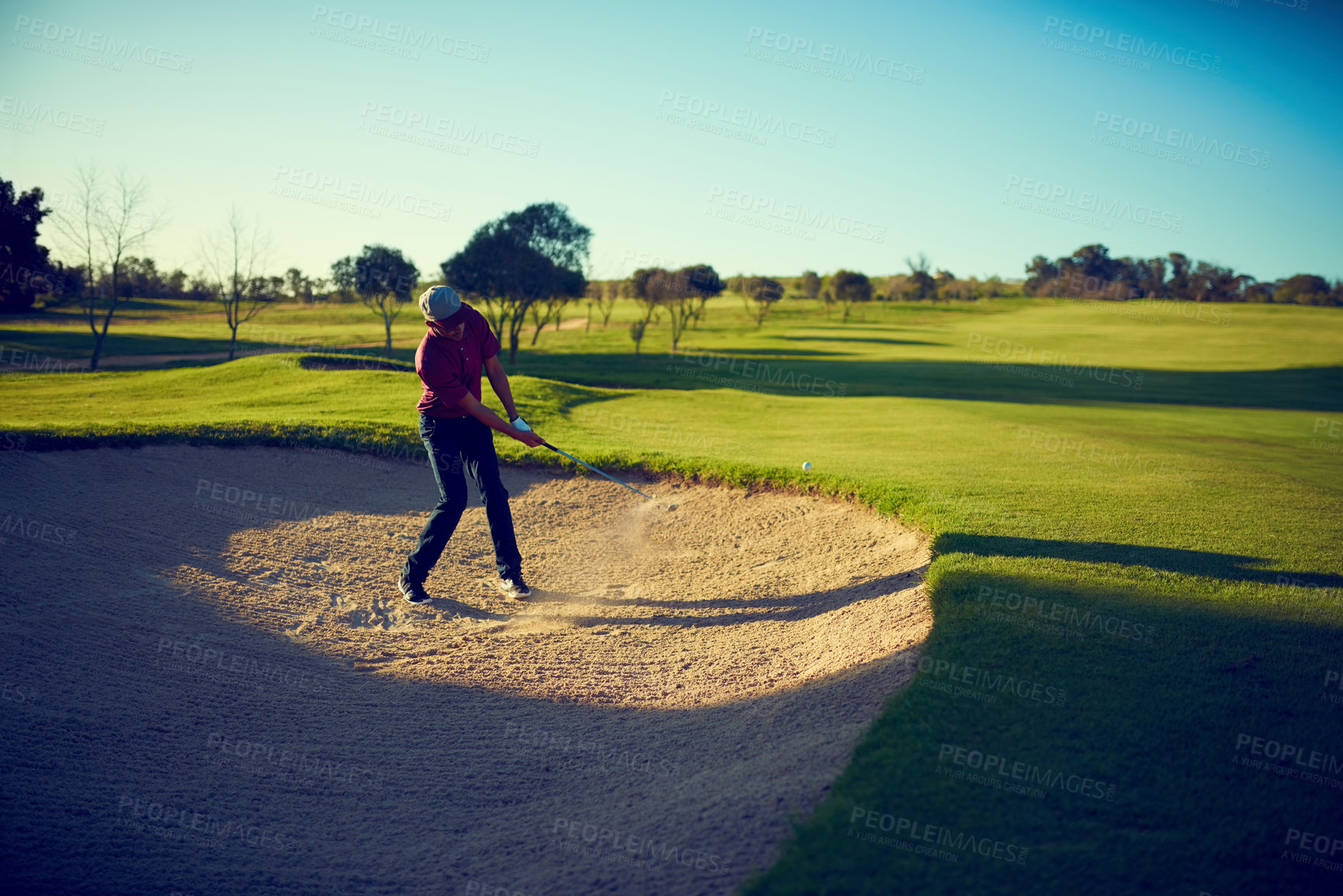 Buy stock photo Shot of a young man hitting the ball out of the bunker during a round of golf