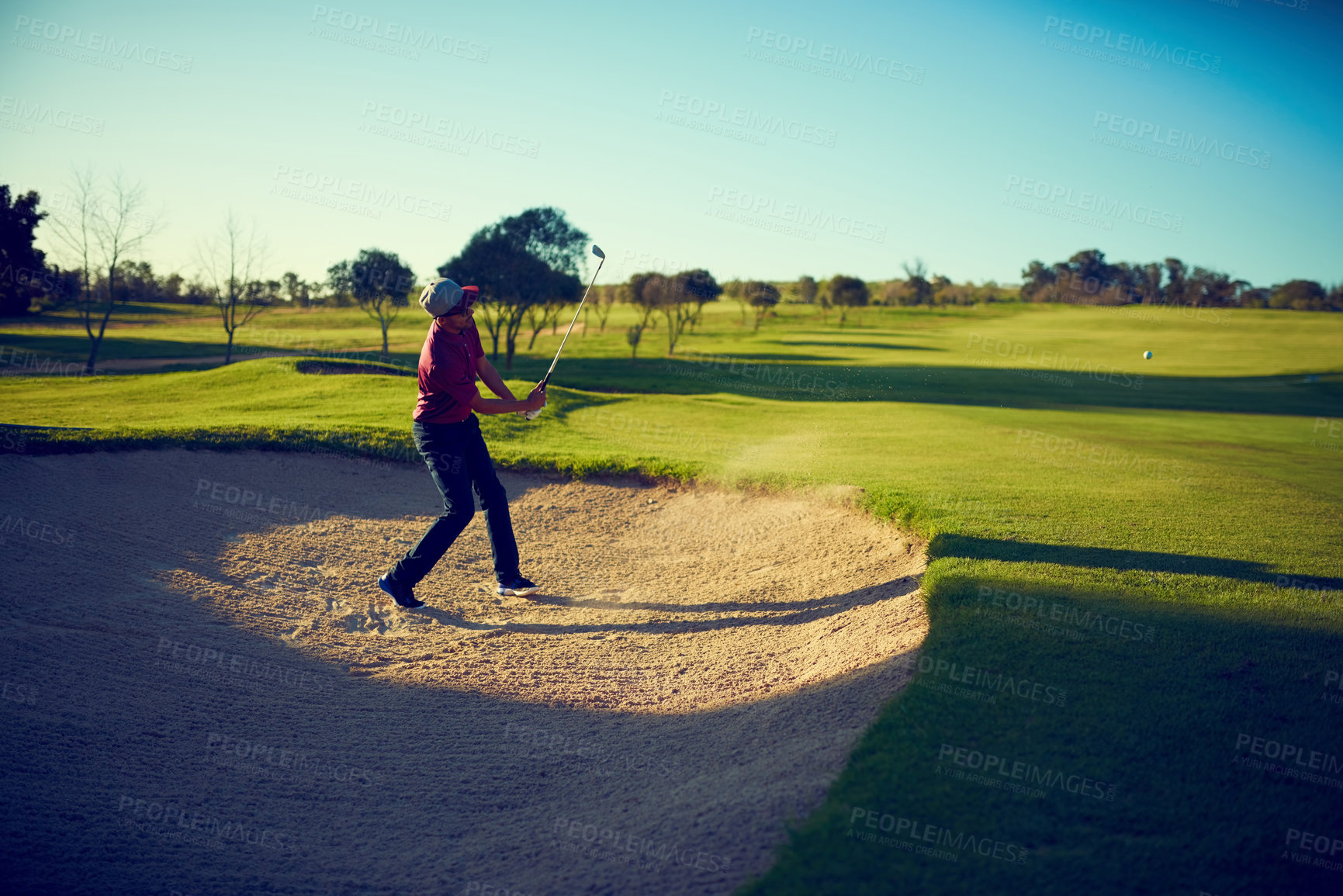 Buy stock photo Shot of a young man hitting the ball out of the bunker during a round of golf