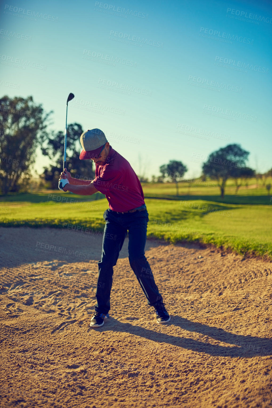 Buy stock photo Shot of a young man hitting the ball out of the bunker during a round of golf