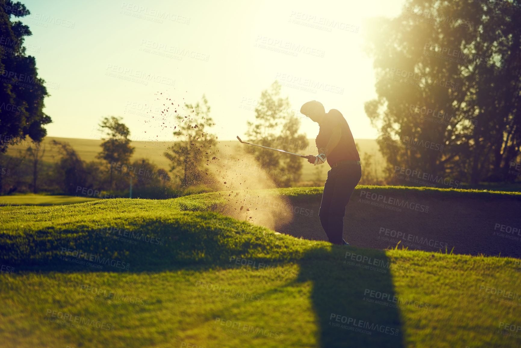 Buy stock photo Shot of a young man hitting the ball out of the bunker during a round of golf