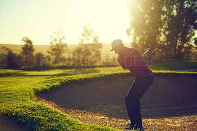 Buy stock photo Shot of a young man hitting the ball out of the bunker during a round of golf