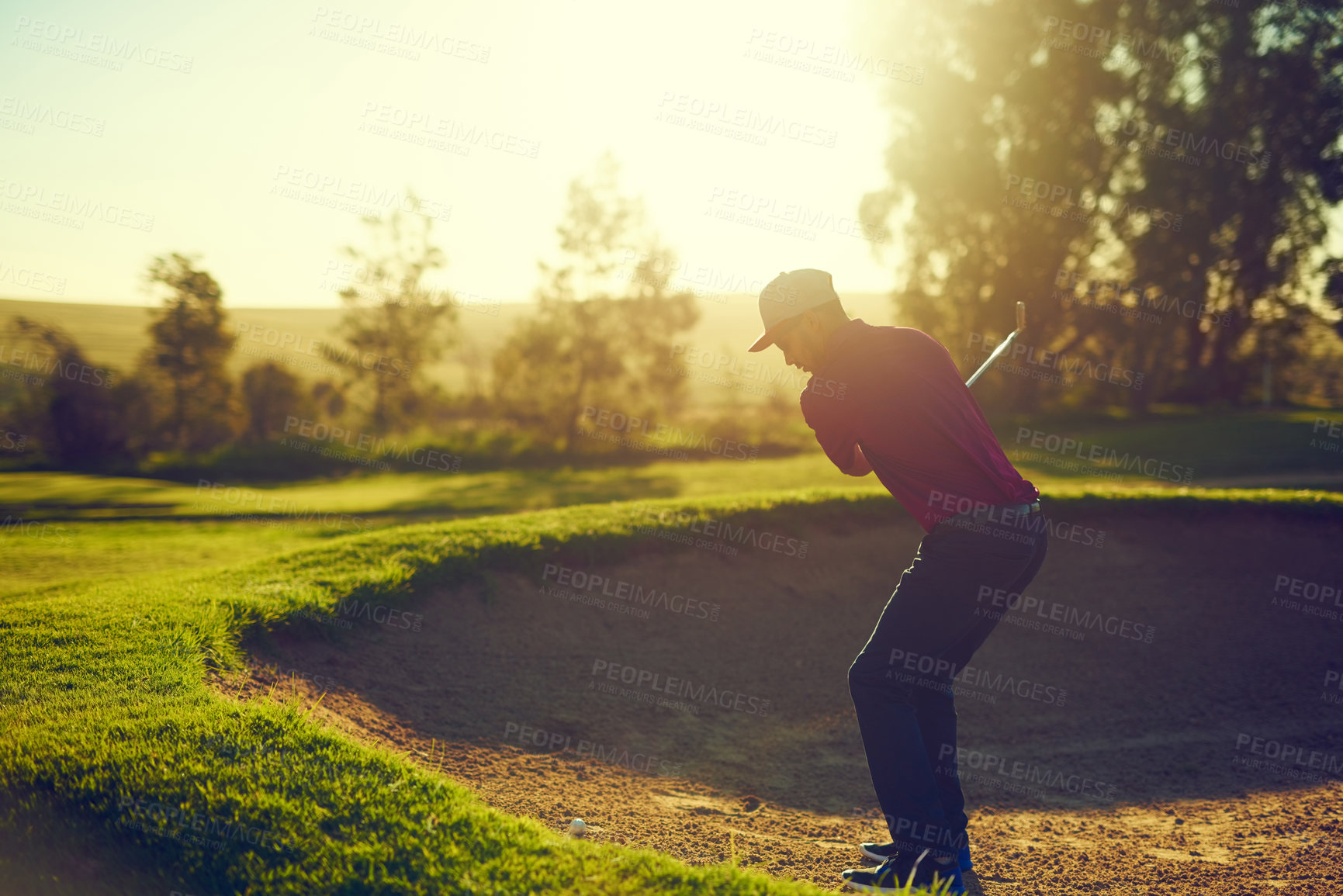 Buy stock photo Shot of a young man hitting the ball out of the bunker during a round of golf