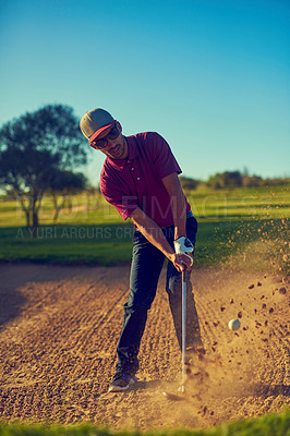 Buy stock photo Shot of a young man hitting the ball out of the bunker during a round of golf