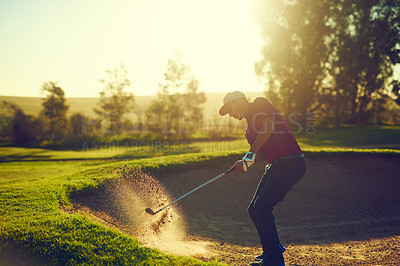 Buy stock photo Shot of a young man hitting the ball out of the bunker during a round of golf