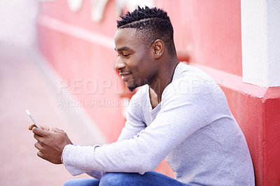Buy stock photo Cropped shot of a young man using his phone while out in the city
