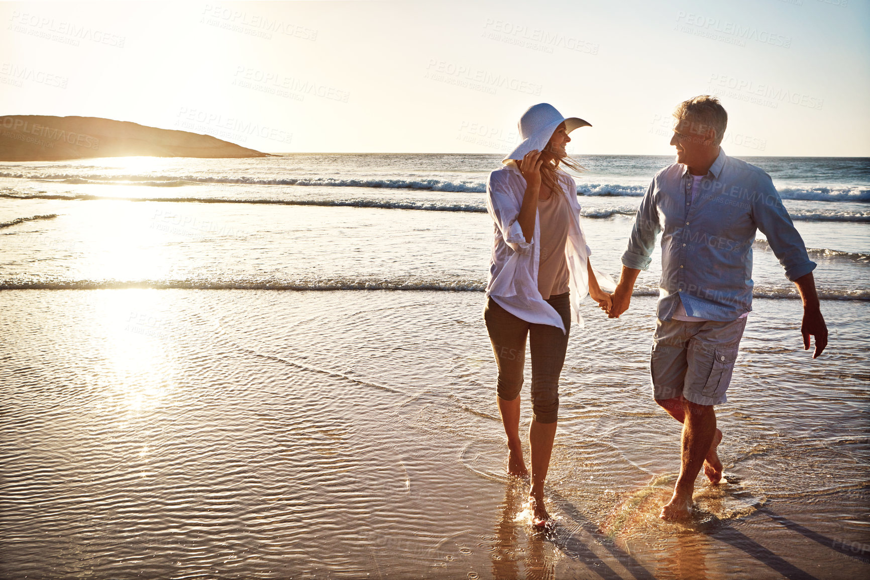 Buy stock photo Senior, happy couple and holding hands on beach at sunset for love, embrace or bonding together in nature. Man, woman or lovers support on outdoor summer holiday by water or ocean coast in sunshine