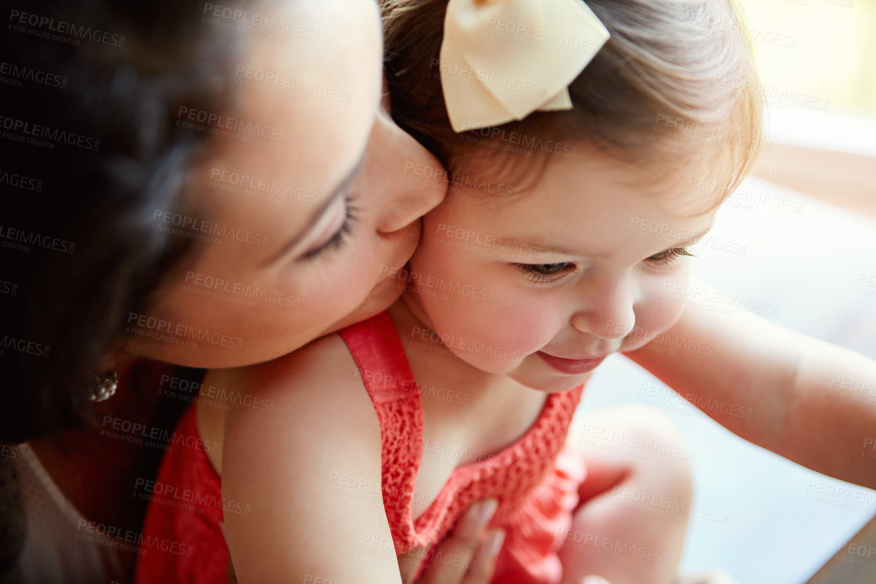 Buy stock photo Shot of a mother giving her adorable little daughter a kiss on the cheek at home