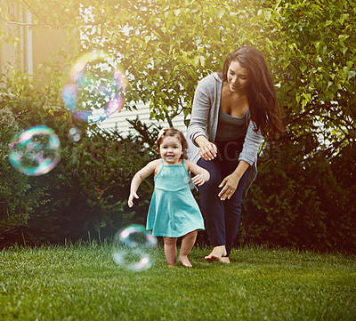 Buy stock photo Shot of a mother and her adorable little daughter playing with bubbles outside