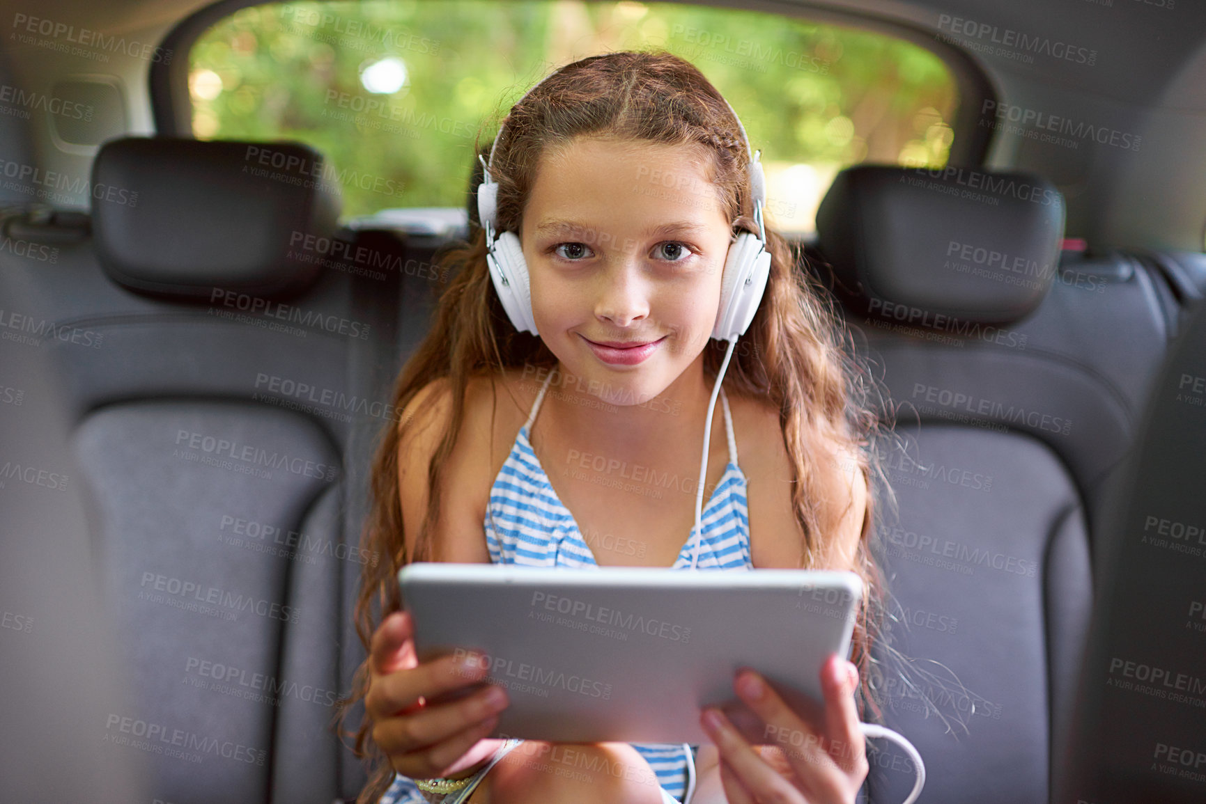 Buy stock photo Shot of a young girl sitting in a car backseat wearing headphones and using a digital tablet
