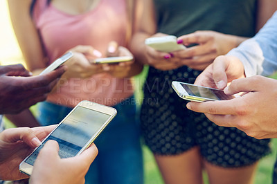 Buy stock photo Cropped shot of a group of friends using their phones together outdoors