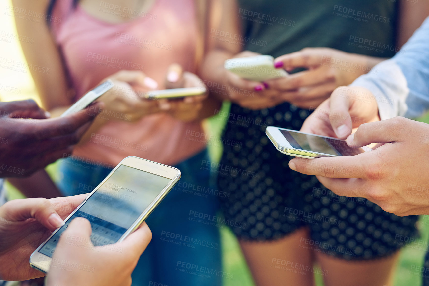 Buy stock photo Cropped shot of a group of friends using their phones together outdoors