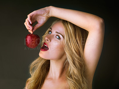 Buy stock photo Studio shot of a gorgeous young woman eating a red apple suggestively against a dark background