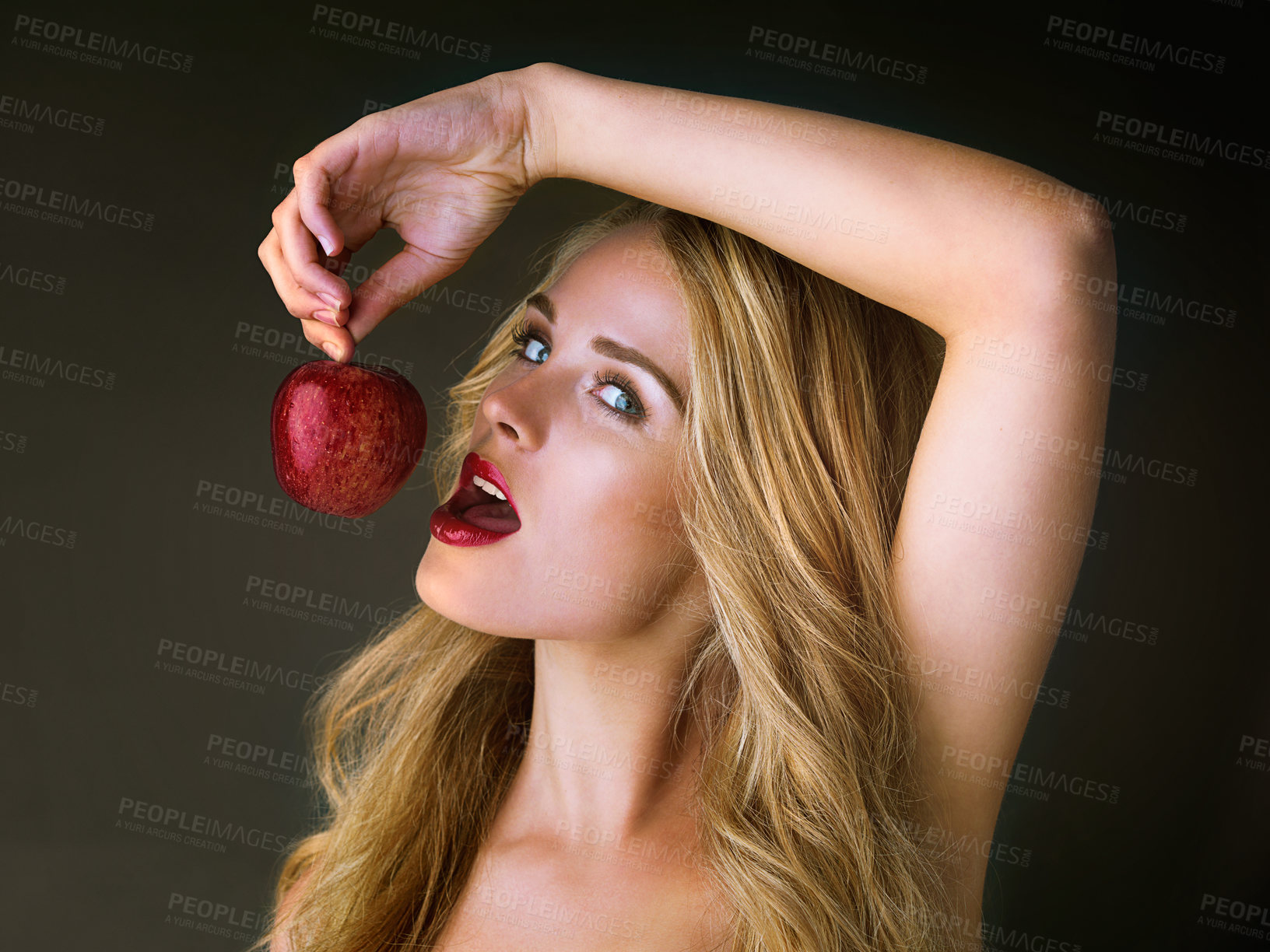 Buy stock photo Studio shot of a gorgeous young woman eating a red apple suggestively against a dark background