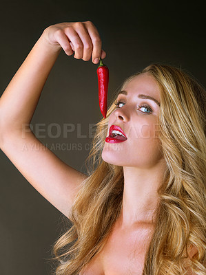 Buy stock photo Studio shot of a gorgeous young woman eating a red chili suggestively against a dark background