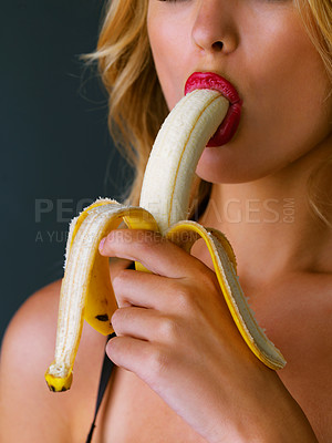 Buy stock photo Cropped studio shot of a young woman eating a banana suggestively against a dark background