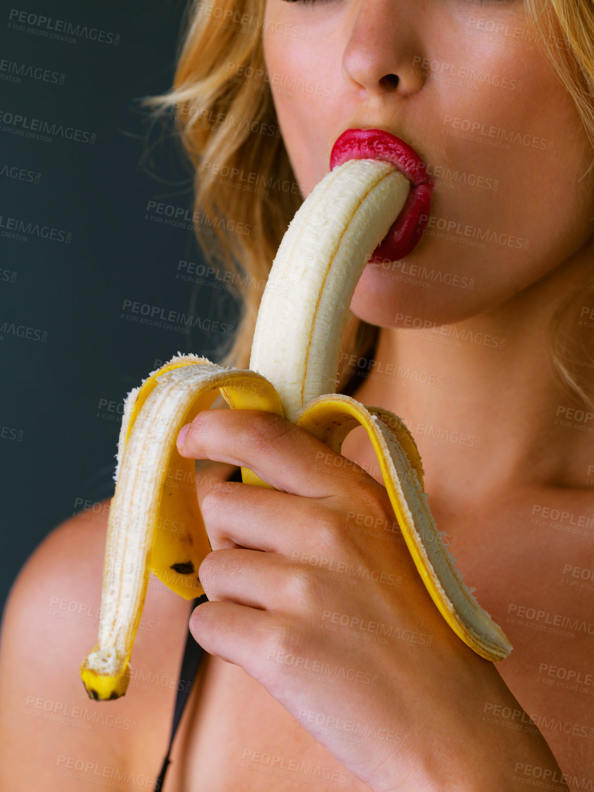 Buy stock photo Cropped studio shot of a young woman eating a banana suggestively against a dark background