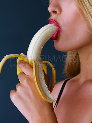 Buy stock photo Cropped studio shot of a young woman eating a banana suggestively against a dark background