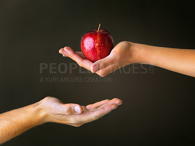 Buy stock photo Cropped studio shot of a woman offering a man a red apple against a dark background