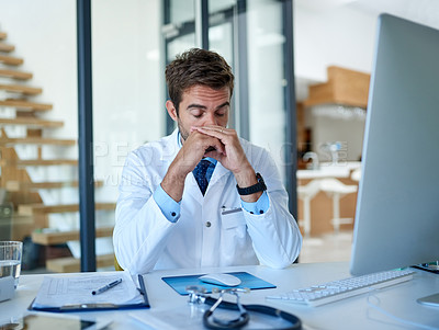 Buy stock photo Cropped shot of a young doctor looking stressed while working in his office
