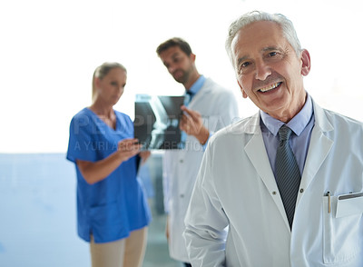 Buy stock photo Portrait of a mature doctor standing in a hospital with his colleagues in the background