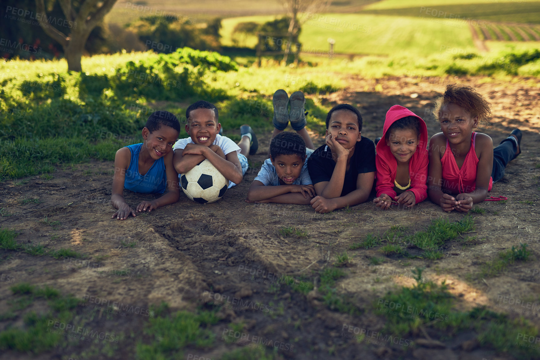 Buy stock photo Kids, happy and lying on ground with soccer ball in field or outdoor for fun, sports and child development. People, boys and girls with smile on portrait for fitness, training and exercise in Brazil