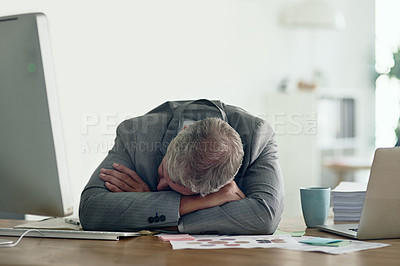 Buy stock photo Shot of an exhausted businessman resting on his arms at his desk