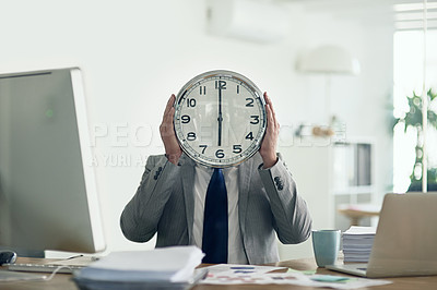 Buy stock photo Shot of an unidentifiable businessman holding a clock in front of his face while sitting at his desk