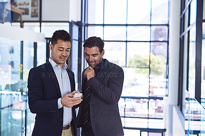 Buy stock photo Cropped shot of two businessmen discussing something on a cellphone in an office