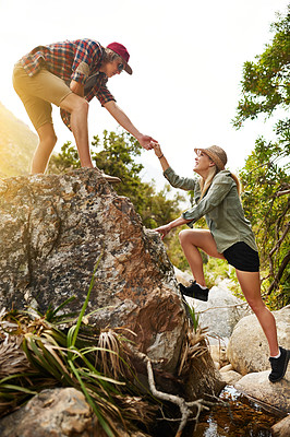Buy stock photo Shot of a young man helping his girlfriend climb up a rock in nature