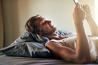 Buy stock photo Cropped shot of a young man texting on his cellphone while lying in bed