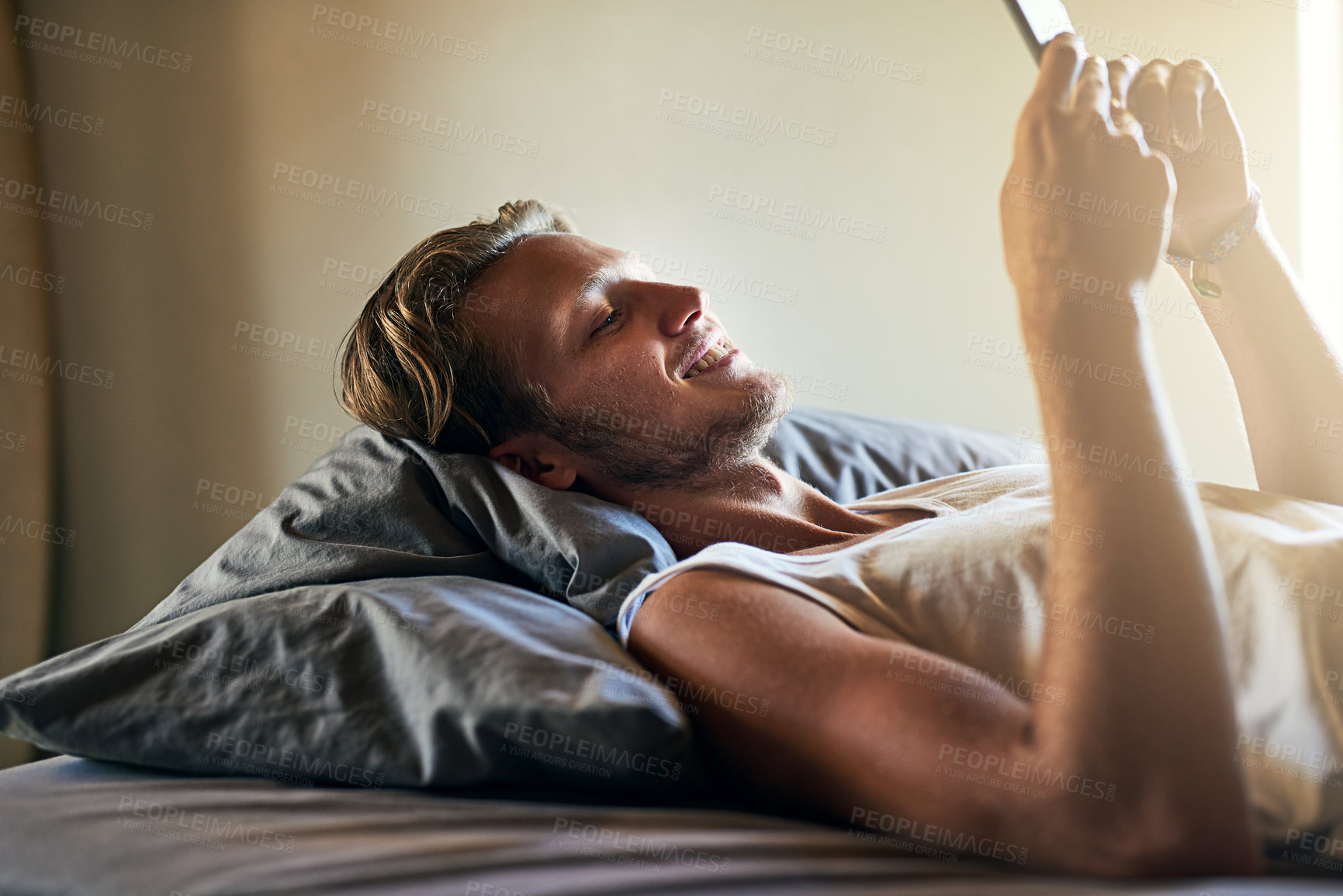 Buy stock photo Cropped shot of a young man texting on his cellphone while lying in bed