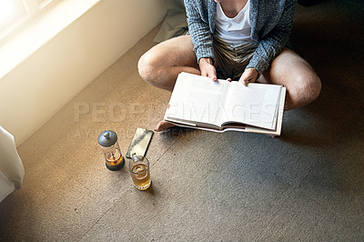 Buy stock photo High angle shot of an unidentifiable young man reading a book at home
