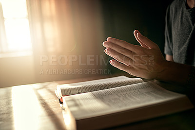 Buy stock photo Cropped shot of an unidentifiable man clasping his hands in prayer over an open Bible