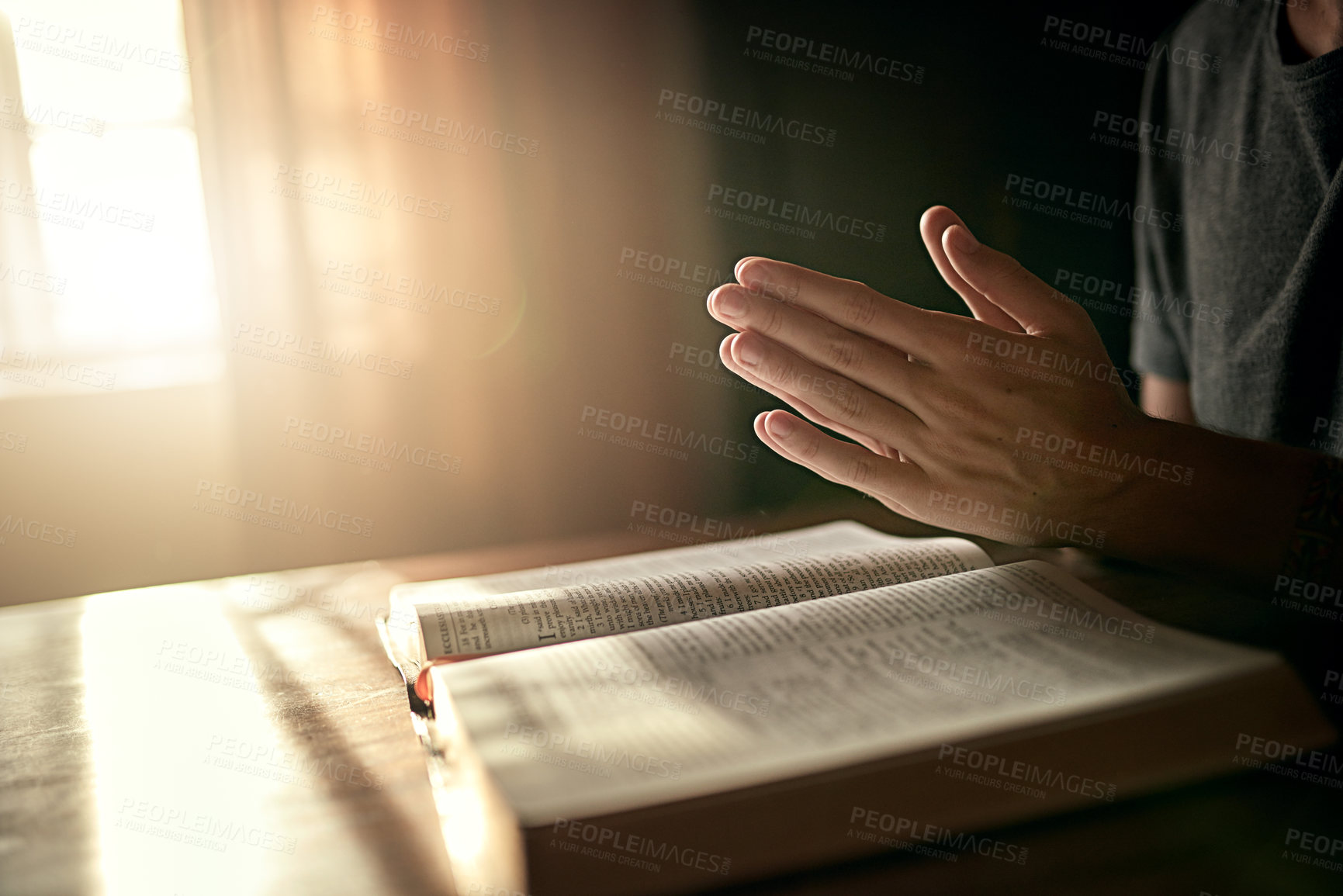 Buy stock photo Cropped shot of an unidentifiable man clasping his hands in prayer over an open Bible