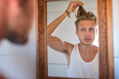 Buy stock photo Cropped shot of a young man looking at his hair in his bathroom mirror