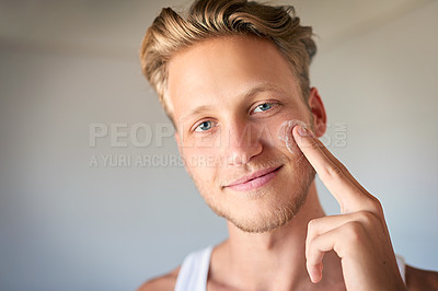 Buy stock photo Cropped shot of a young man applying moisturizer to his face