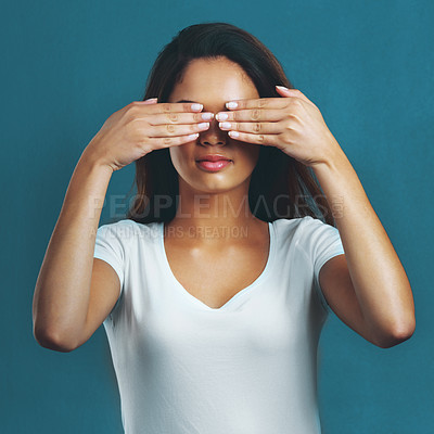Buy stock photo Studio shot of an attractive young woman covering her eyes against a blue background