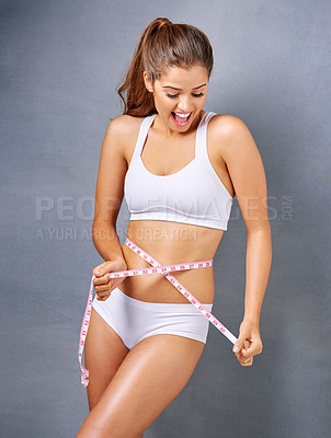 Buy stock photo Studio shot of an attractive young woman measuring her waist against a grey background