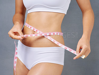Buy stock photo Studio shot of a young woman measuring her waist against a grey background