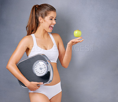 Buy stock photo Studio shot of an attractive young woman holding a scale and throwing an apple against a grey background