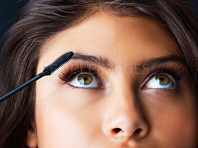 Buy stock photo Shot of a gorgeous young woman applying mascara against a dark background