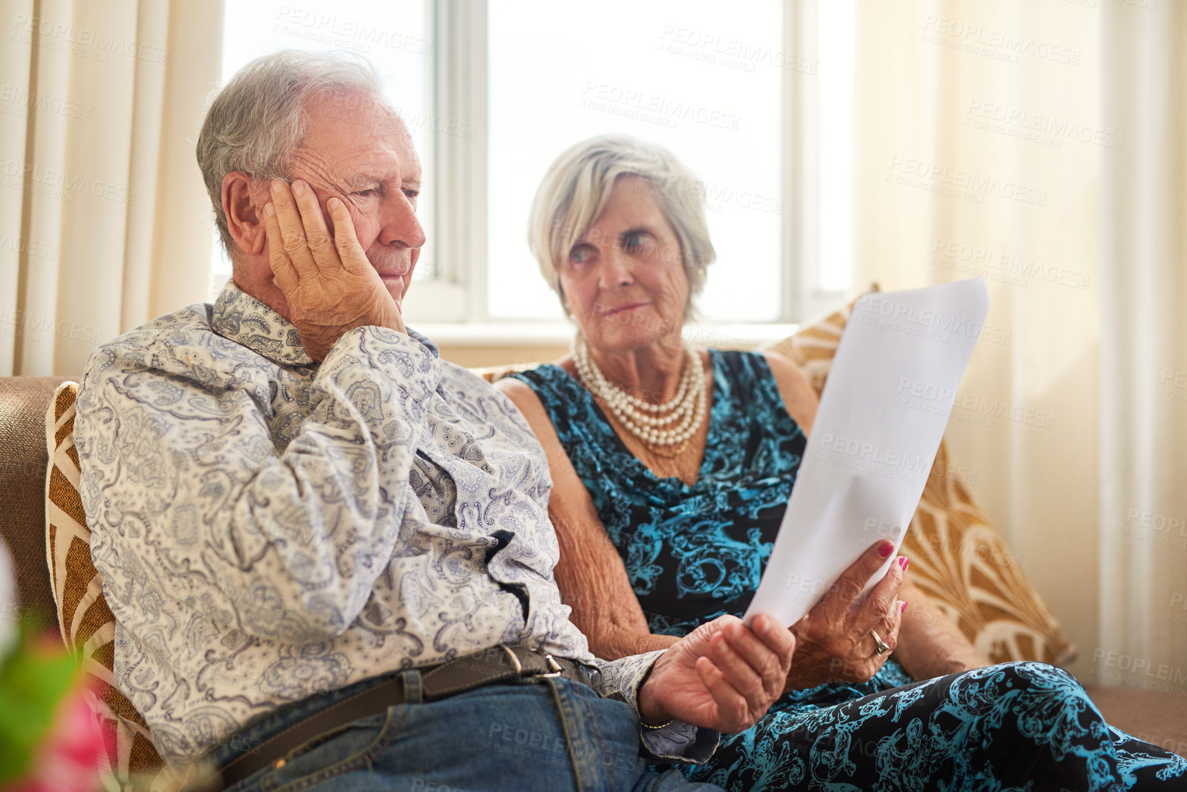 Buy stock photo Shot of a senior couple going through their paperwork together at home and looking worried