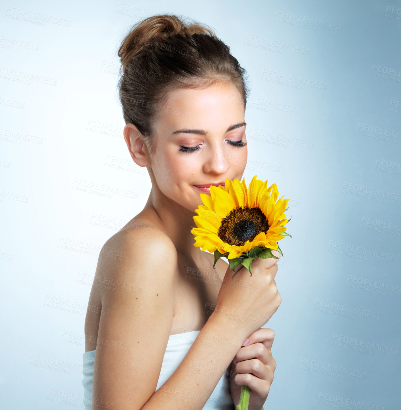 Buy stock photo Sunflower, smelling and woman in studio with makeup, organic and beauty facial makeover. Glow, cosmetics and female person with yellow floral plant for cosmetology face routine by blue background.