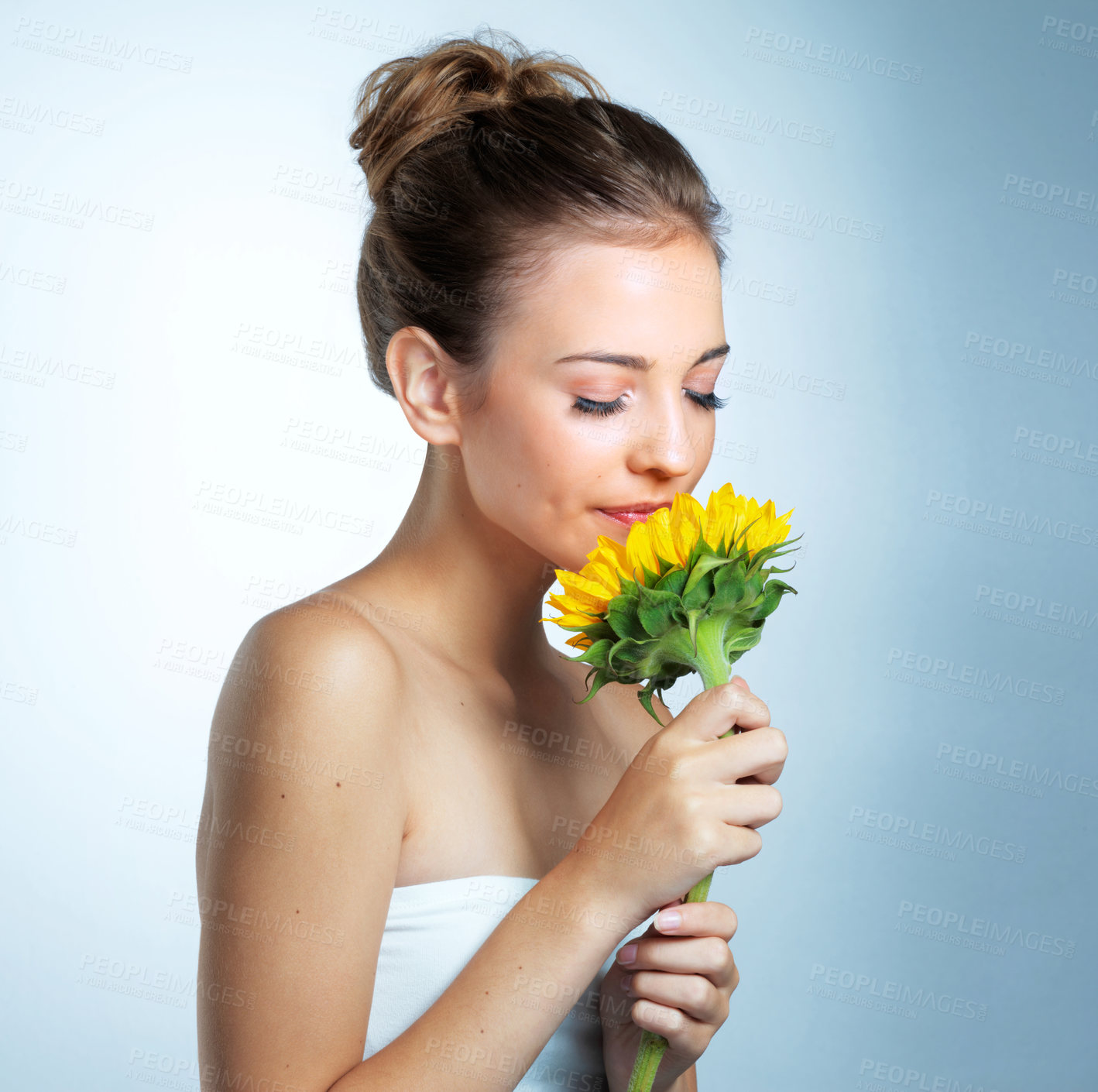 Buy stock photo Skincare, smelling and woman with bouquet of sunflowers in studio for natural, beauty and facial routine. Health, face and female person with floral plants for organic dermatology by blue background.