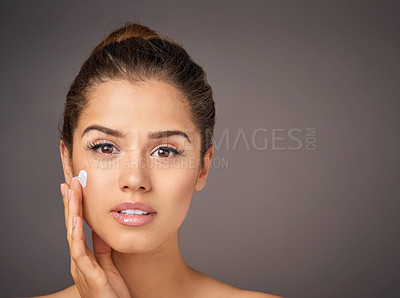 Buy stock photo Studio portrait of a beautiful young woman applying moisturizer to her face against a gray background