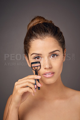 Buy stock photo Portrait of a beautiful young model using an eyelash curler to shape her lashes in studio